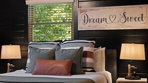 Una cama con varias almohadas, una ventana con persianas y un cartel en la pared que dice 'Dream & Sweet'.