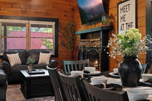 A cozy room with a fireplace, a television mounted on the wall, and a dining area with a table set for two.