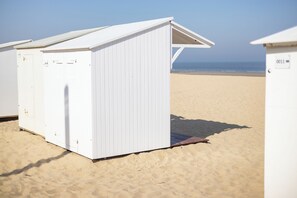 Uma estrutura branca à beira-mar com telhado inclinado, porta e uma pequena janela.