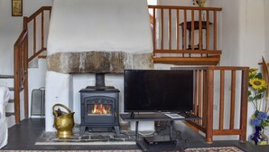 A cozy living room with a stone fireplace, a television, and a wooden staircase. - 2 bedroom accommodation in Camelford (Camelford)