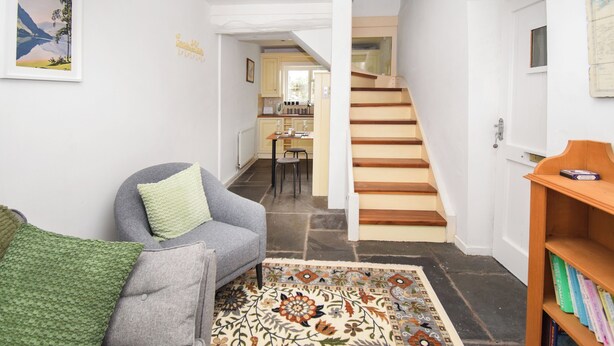 A living room with a grey sofa, a patterned rug, a wooden staircase, and a bookshelf with books. - 1 bedroom accommodation in Keswick (Keswick)