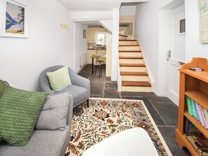 Una sala de estar con un sofá gris, un tapete estampado, una escalera de madera y una estantería llena de libros.