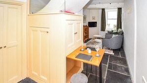 A compact kitchen with a dining area, featuring a small table with chairs, a stool, and a television mounted on the wall. - 1 bedroom accommodation in Keswick (Keswick)
