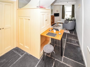 A compact kitchen with a dining area, featuring a small table with chairs, a stool, and a television mounted on the wall.
