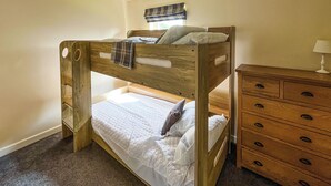 A bunk bed with a wooden frame, a bedside table with drawers, and a lamp on a dresser. - 3 bedroom accommodation in Brigg (Brigg)
