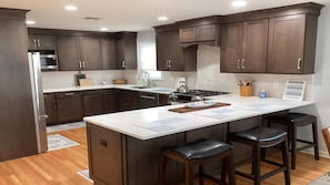 A modern kitchen with dark wood cabinets, a stainless steel refrigerator, a gas stove, and a large island with bar stools.