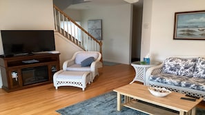 A living room with a television, wicker chairs, a sofa, a wooden coffee table, and a staircase.