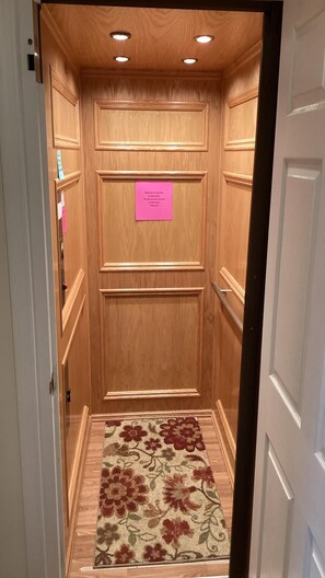 Un ascenseur étroit aux parois lambrissées et une enseigne rose sur la porte.