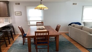 A dining area with a wooden table, chairs, a hanging light fixture, and a window with blinds. - 4 bedroom accommodation in Surf City (Surf City)