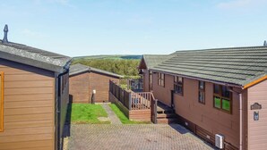 A courtyard with wooden buildings, a paved walkway, and a grassy area. - 2 bedroom accommodation in Ilfracombe (Ilfracombe)