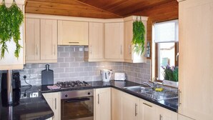 A modern kitchen with light wooden cabinets, a black countertop, a gas stove, an oven, and hanging plants. - 2 bedroom accommodation in Ilfracombe (Ilfracombe)