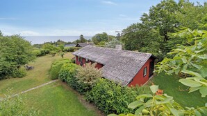 Una casa vermella amb teulada inclinada, envoltada de vegetació exuberant i una vista despejada del mar.