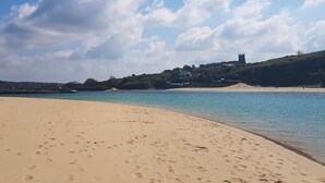 Una playa con huellas que conducen al agua, un cielo despejado y una colina distante con edificios.