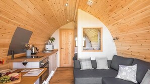 Interior acogedor de una cabaña con techo de madera, un comedor con una mesa preparada para dos personas y un sofá gris con cojines.