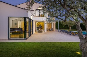 Een modern huis met een glazen gevel, een zwembad en terrasmeubels.