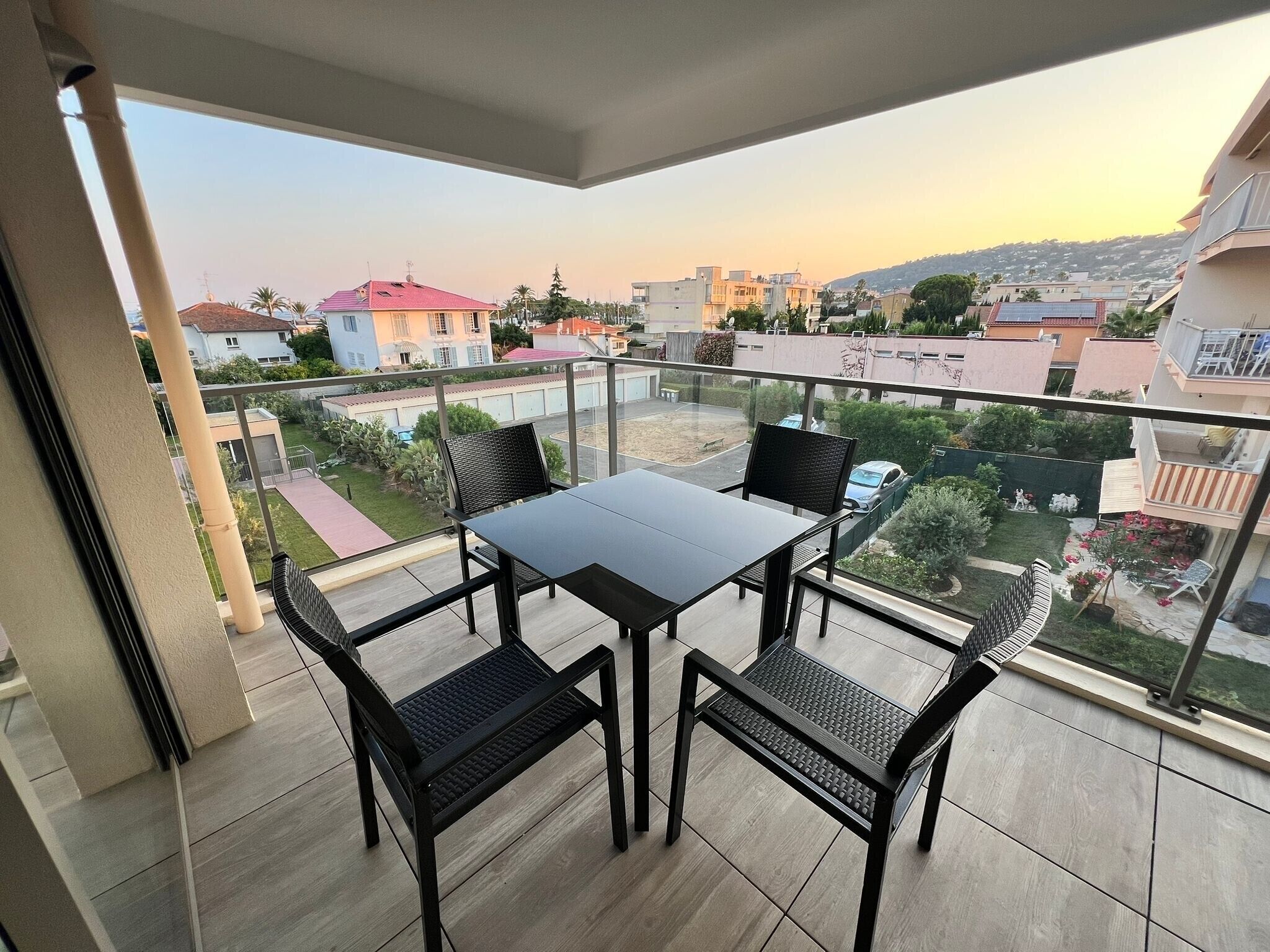 A balcony with a table and chairs, offering a view of a residential area with houses and greenery.