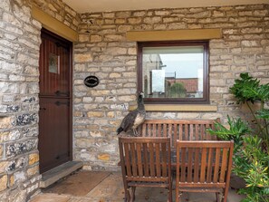 Una cabaña de piedra con puerta de madera, un banco y una ventana con vistas a un jardín.