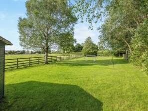 A grassy field with a wooden fence, trees, and a small building.