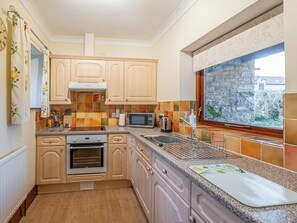 Una cocina con armarios de madera, microondas, estufa y ventana con vista a un muro de piedra.
