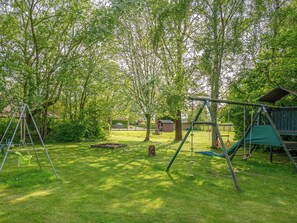 Un parque infantil con columpios y estructuras para escalar, rodeado de árboles y césped.