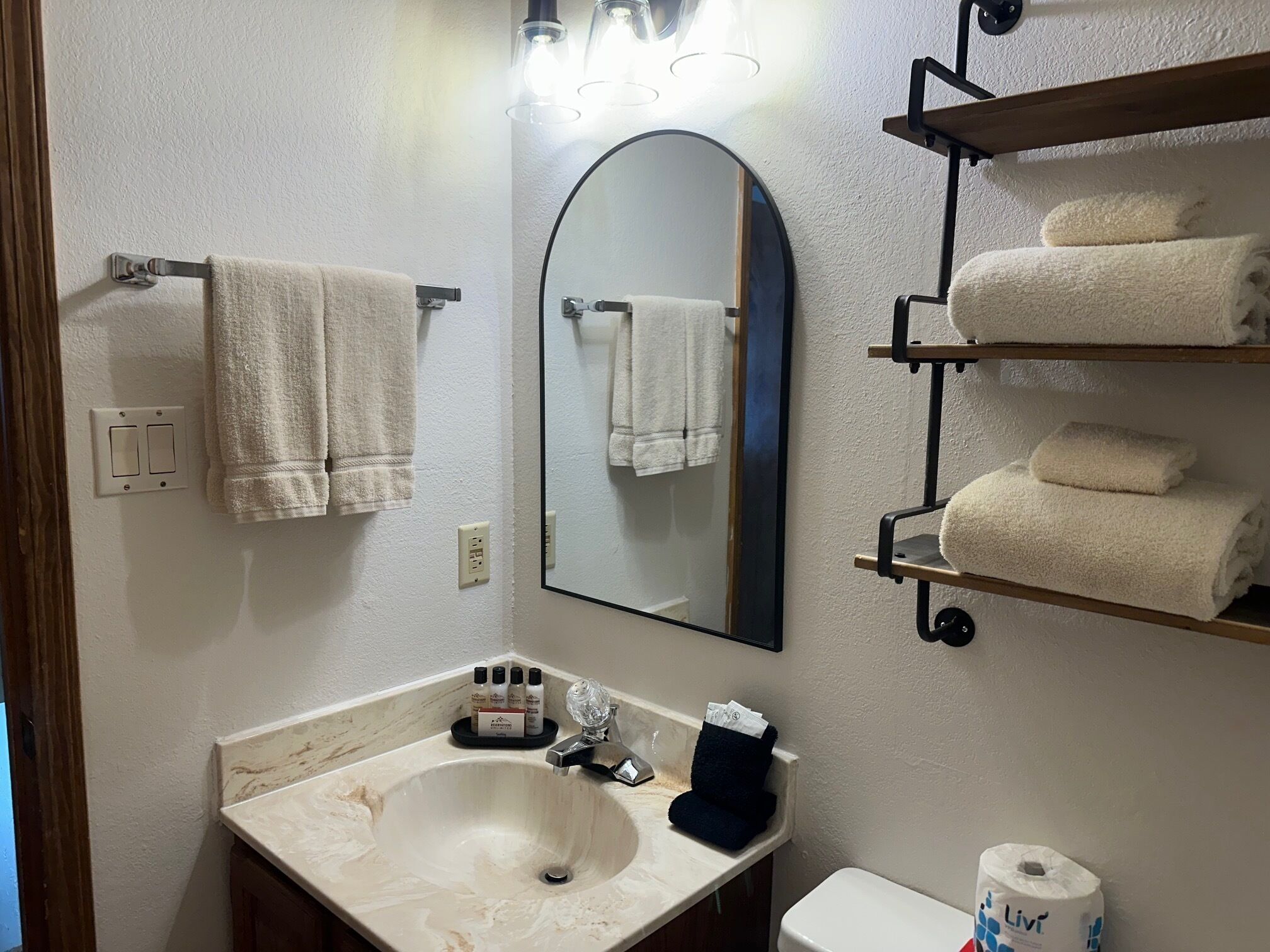Une salle de bain équipée d’un lavabo, d’un miroir, d’un porte-serviettes et d’étagères où sont rangées les serviettes.