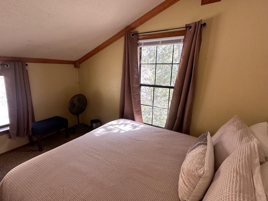 Un dormitorio con una cama grande, una ventana con cortinas, un ventilador y un banco junto a la ventana.