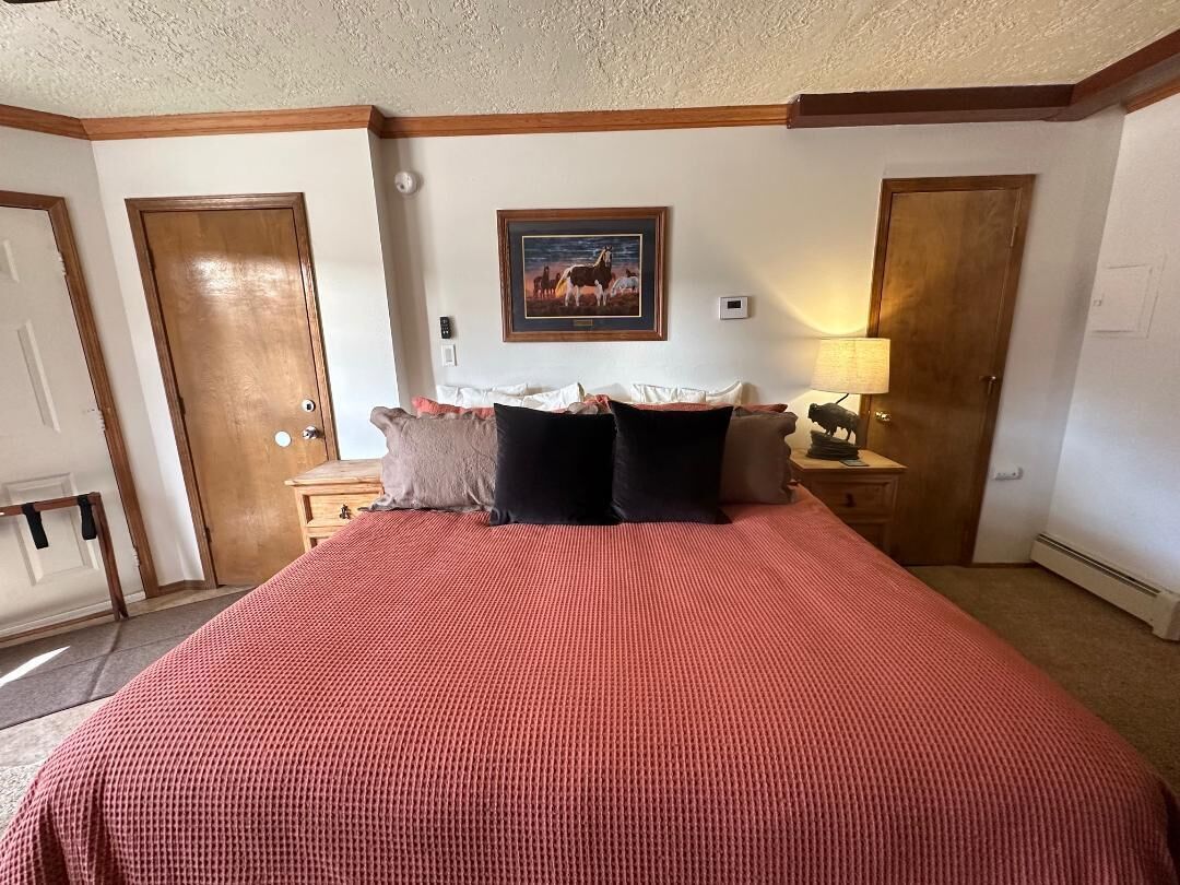 A bedroom with a large bed, two nightstands, a framed picture on the wall, and wooden doors.