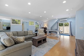 A spacious living room with a sofa, armchair, coffee table, and a pool table.