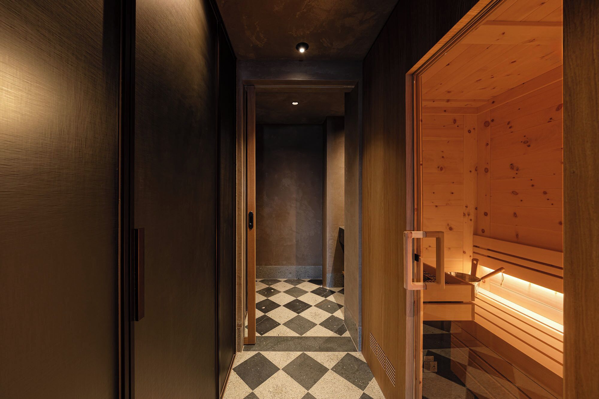 Un pasillo con piso a cuadros que conduce a un área de sauna con paredes de madera y un banco.