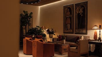 A warmly lit living room with a sofa, ottomans, a coffee table, and two framed religious paintings on the wall.