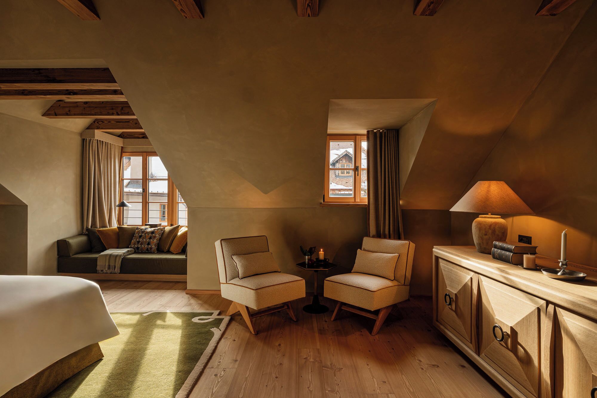 Una habitación acogedora con una cama, dos sillones, una mesita con una vela y un aparador con libros.