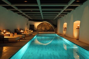 A modern indoor pool with a clear blue water feature, a stone wall, and seating areas with soft lighting. - Castel Badia (San Lorenzo di Sebato)