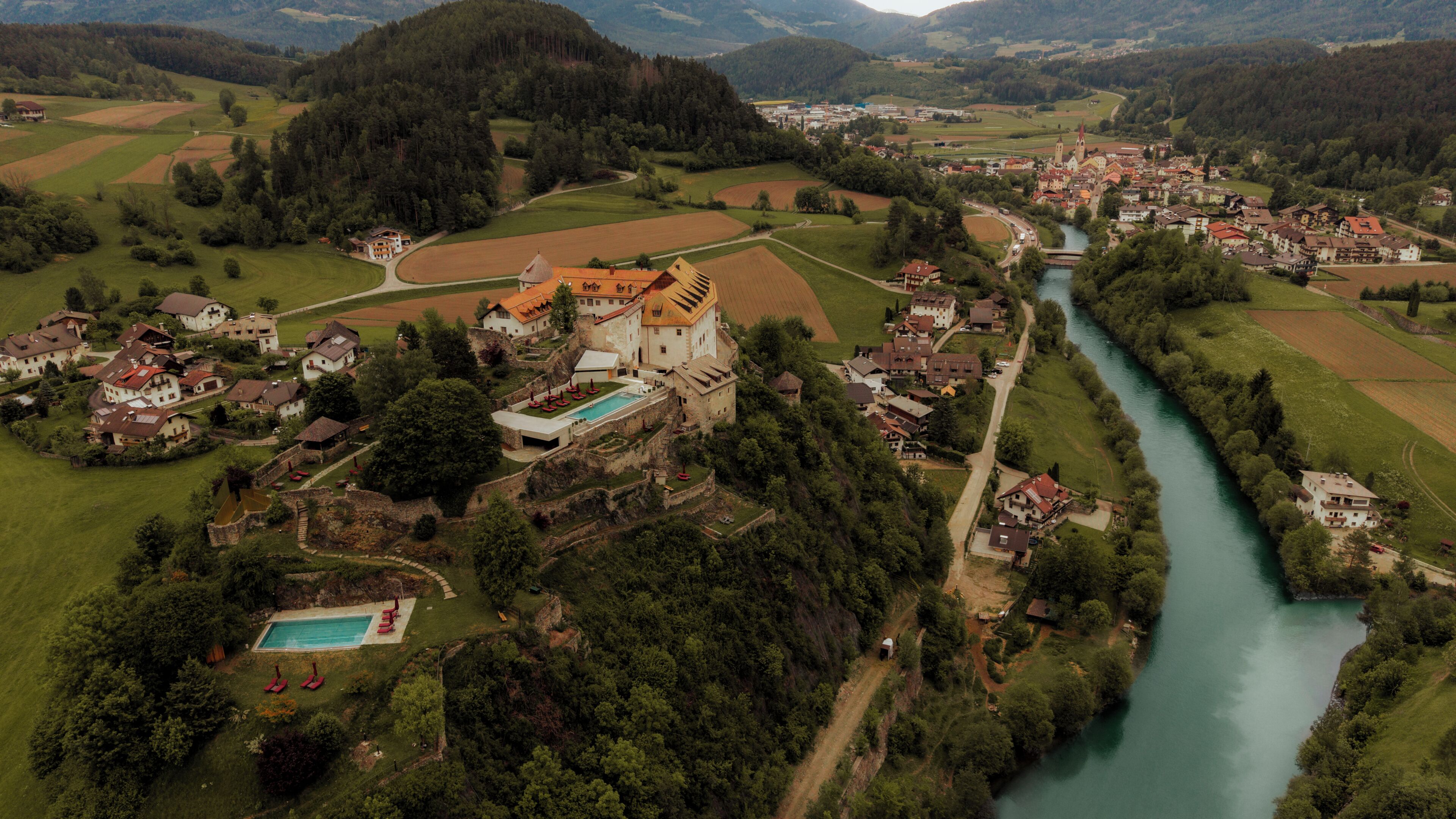 Vista aérea de un pueblo con un castillo, un río y campos circundantes.