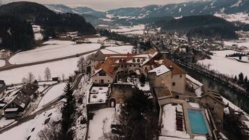 A historic building with a courtyard and a swimming pool, surrounded by snow-covered landscapes and mountains.