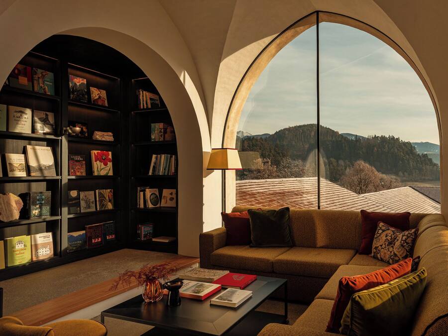 Una sala de estar acogedora con una amplia estantería, un sofá cómodo y vistas a un paisaje montañoso a través de un ventanal arqueado.