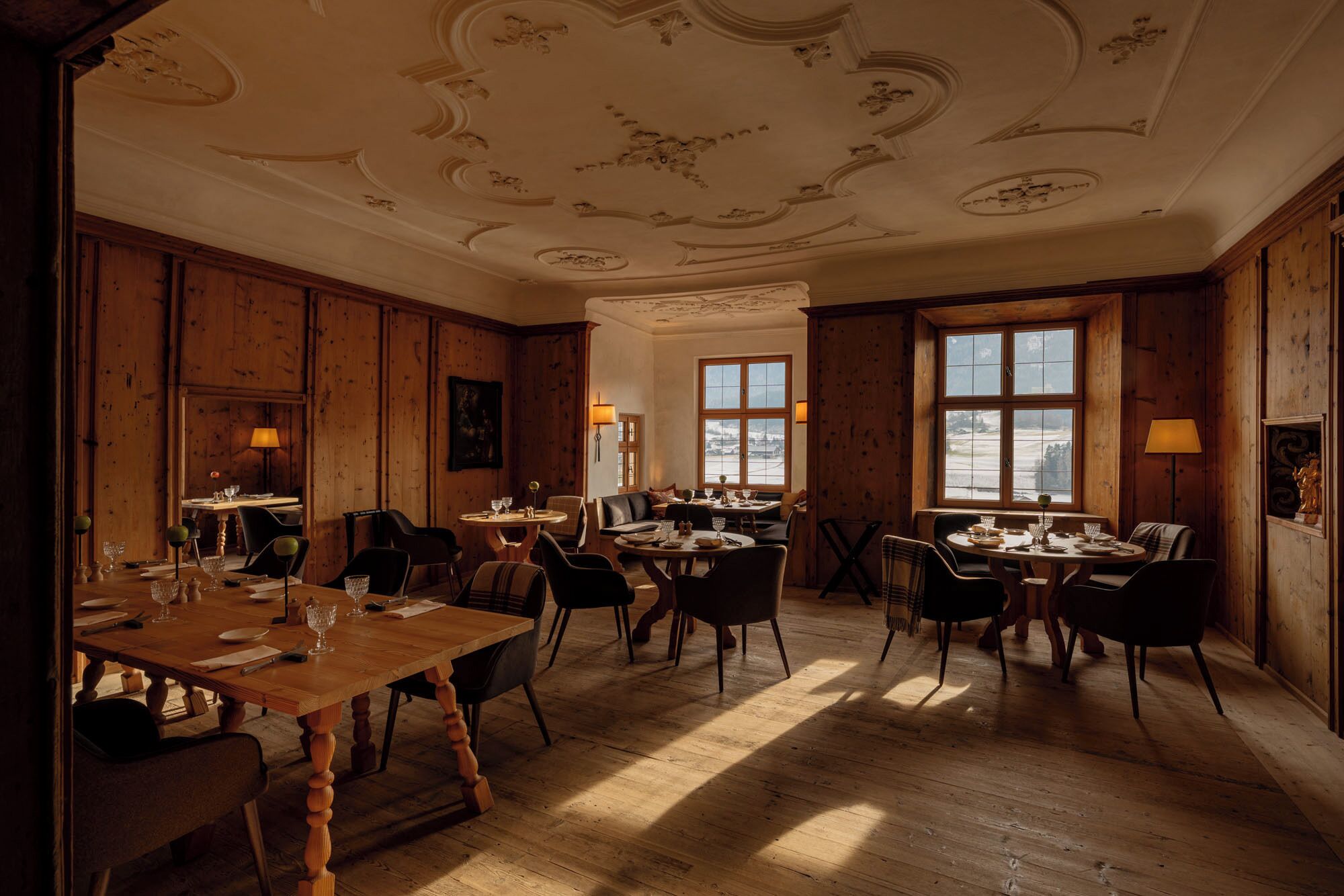 Comedor con paneles de madera, una gran mesa de madera y dos ventanas que dejan entrar luz natural.