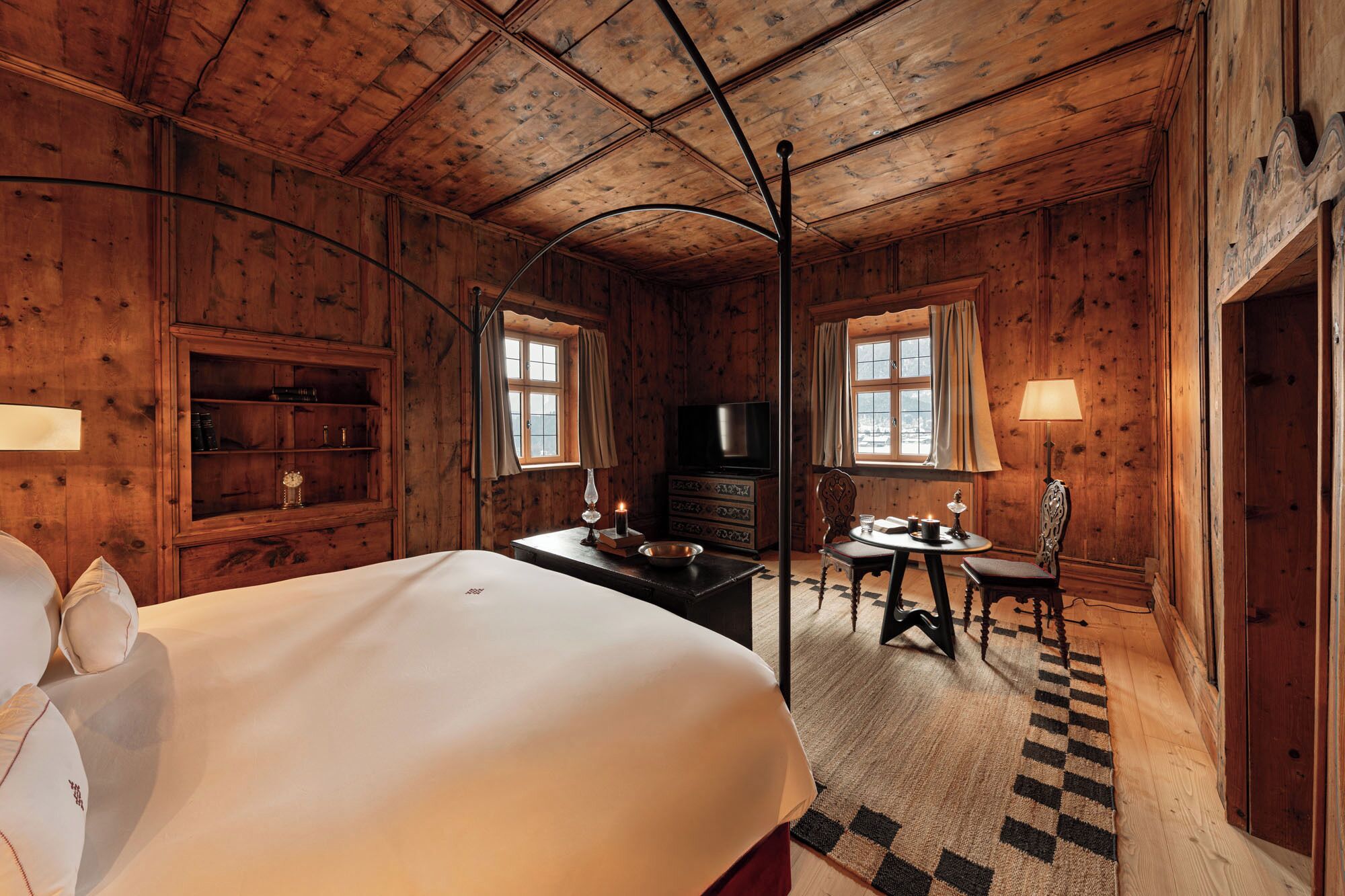 A wooden room with a bed, a TV, a table, and a chair.