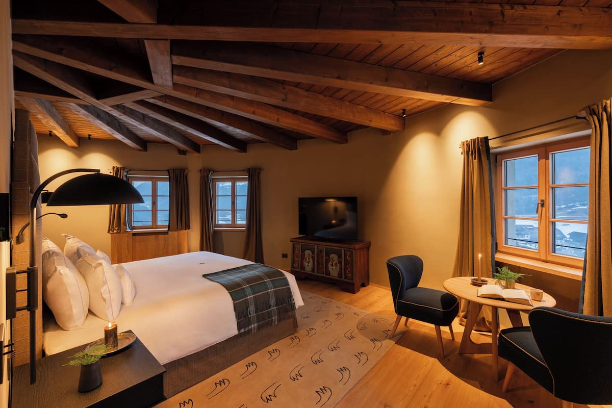 A cozy bedroom with a bed, a TV, a desk with a chair, and a window with curtains.