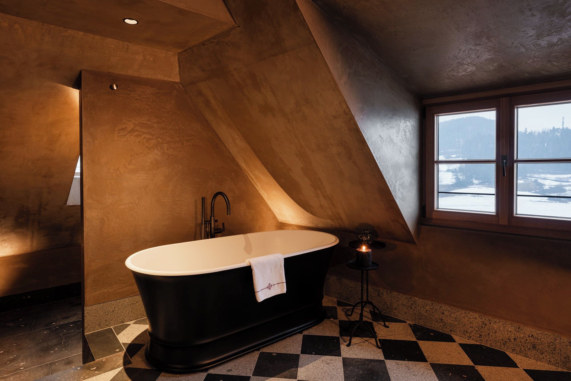 Un baño moderno con una bañera independiente, un ventanal con vistas a un paisaje nevado y un suelo a cuadros.