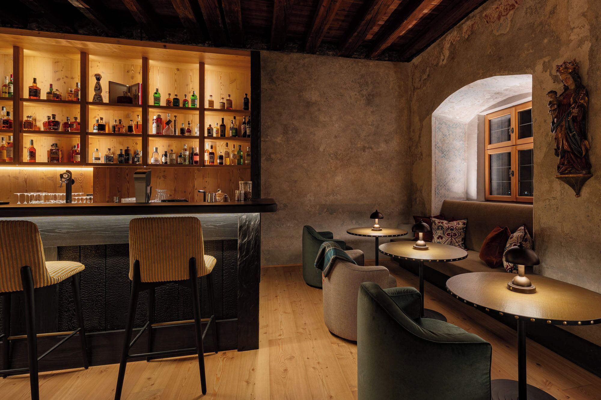 Zona de bar con estantes de madera llenos de botellas, barra y asientos que incluyen sillas y un sofá.
