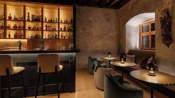 Zona de bar con estantes de madera llenos de botellas, barra y asientos que incluyen sillas y un sofá.