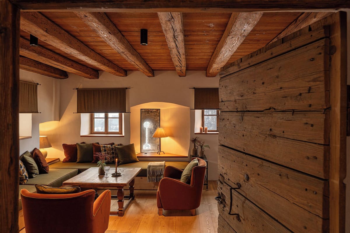 A cozy room with a wooden ceiling, a sofa set, a table with a candle, and a large window.