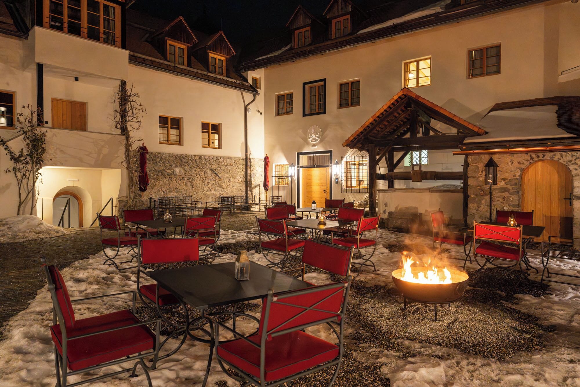 An outdoor seating area with tables and chairs, a fire pit, and a stone wall.