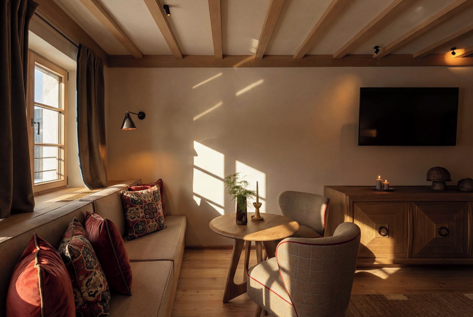 Un salon confortable avec un canapé, un fauteuil et une petite table. Un téléviseur est fixé au mur, et il y a une fenêtre avec des rideaux.
