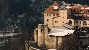 A historic building with a stone tower and multiple windows, surrounded by a forested area. - Castel Badia (San Lorenzo di Sebato)