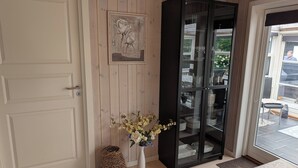 A room with a white door, a black cabinet with glass doors, a wicker basket, and a vase with flowers. - Charming cottage with large fenced garden (Løgstør)