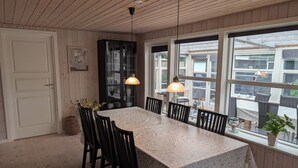A dining area with a wooden ceiling, a large table with chairs, and a view through large windows. - Charming cottage with large fenced garden (Løgstør)