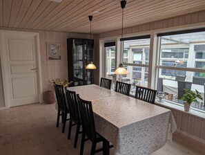 A dining area with a table, chairs, pendant lights, and a view through large windows. - Charming cottage with large fenced garden (Løgstør)
