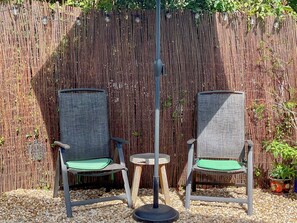 Deux chaises en osier avec des coussins verts, une petite table ronde et une clôture en bambou en arrière-plan.