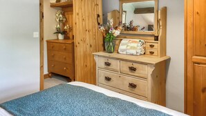A bedroom with a bed, a wooden dresser with drawers, a mirror, and a vase with flowers. - The Old Post House Annex - UK50190 (Axbridge, near Weare)